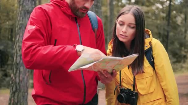 Close up of caucasian man showing girl in forest road on paper map. Young couple of tourists looking for way out of park. — Stock Video