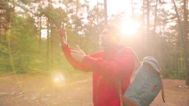 Jonge Kaukasische man met reisrugzak wandelt in het bos in zonnige dag en houdt zijn hand vast met smartphone op zoek naar mobiel netwerk. — Stockvideo