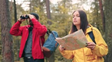 Sarı ceketli genç bir kadın harita tutuyor ve erkek arkadaşından tavsiye istiyor. İki turist ormanda doğru yolu arıyor..