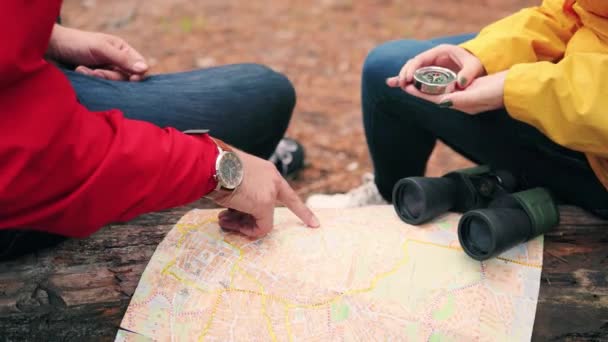 Primer plano de los turistas hombres y mujeres sentados en el bosque y utilizando el mapa y la brújula tratando de pavimentar la ruta de la caminata. — Vídeo de stock