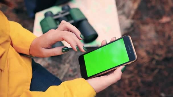 Primo piano di donna seduta su legno log in foresta sullo sfondo di binocoli e utilizzando mobile esplora mappe offline. Vista dall'alto. Schermo verde. — Video Stock