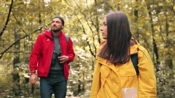 Twee gelukkige toeristen wandelen in het bos en genieten van de natuur. mooi Kaukasisch meisje kijkt rond glimlachen terwijl guy kijkt door verrekijker. — Stockvideo