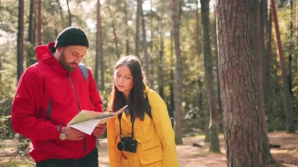Portrait of young stylish couple of tourists standing in woods and studying map looking at camera and smiling. — Stock Video