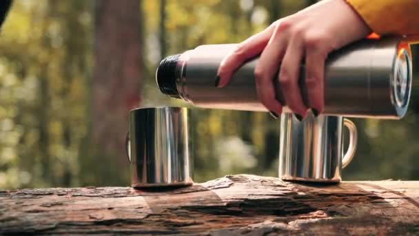 El primer plano de la muchacha vierte la bebida caliente en la taza de viaje que está parada en el tronco en bosques. Concepto de picnic al aire libre en caminata. — Vídeos de Stock