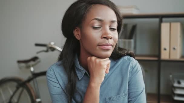 Dekat gadis muda african Amerika yang cantik dengan kemeja denim duduk di kantor modern dan tersenyum di depan kamera. — Stok Video