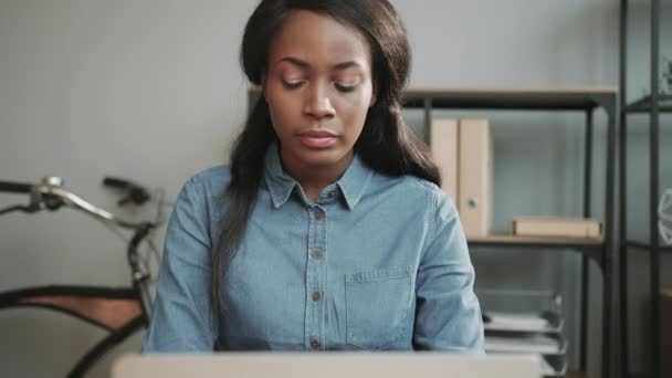 Jovem bela mulher afro-americana em camisa jeans trabalha no escritório e sentado à mesa sente dor aguda no pescoço. — Vídeo de Stock