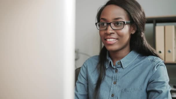 Retrato de una trabajadora afro-americana feliz con gafas sentadas en el escritorio trabajando en la computadora. Trabaje con el cliente en línea. — Vídeos de Stock