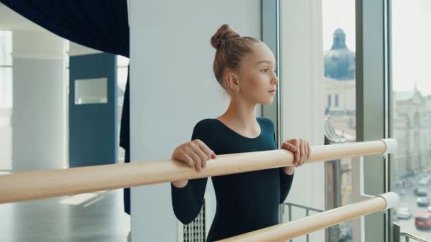 Portret van een klein meisje dat bij het raam op de choreografische school staat en glimlacht terwijl ze naar de camera kijkt. Ballet school. — Stockvideo