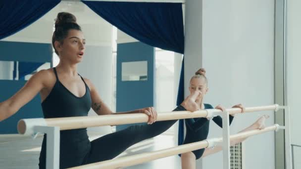 Jovem professor de ginástica bonita está envolvida em classe com a menina e juntos executar curvas nas pernas na máquina de balé. — Vídeo de Stock