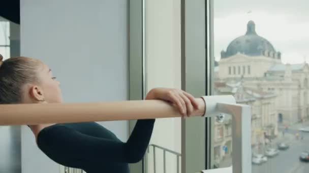 Little girl in black sports swimsuit is doing gymnastics by leaning back with outstretched hand. Warm-up before class. — Stock Video