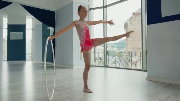 Talangfull liten flicka i rosa kostym tåg innan prestanda och står på ett ben snurrar gymnastik cirkel. — Stockvideo
