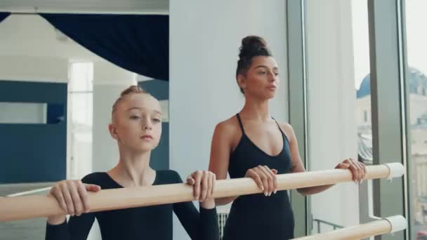 Młoda piękna nauczycielka baletu robi obrót głowy razem z małą uczennicą, a następnie patrzy w uśmiech aparatu. — Wideo stockowe
