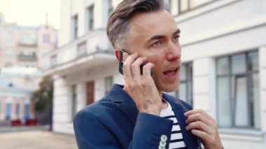 Yakışıklı, orta yaşlı, sokakta yürüyen ve cep telefonuna cevap veren beyaz bir adam. İş adamı dışarıda dolaşıyor ve cep telefonuyla konuşuyor. Telefonda konuşan meşgul bir erkek..