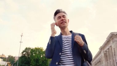 Beyaz tenli, orta yaşlı, yakışıklı bir adamın telefon numarasını çevirmesi ve araması görünüyor. Açık havada. İş adamı cep telefonuyla konuşuyor ve sokakta gülümsüyor. Erkek telefonda konuşuyor. Konuşma.