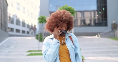 Kıvırcık saçlı, maskeli, şehir sokağında yürüyen ve cep telefonuyla konuşan Afro-Amerikalı genç, şık, hippi bir kadın. Şehirde güzel bir bayan cep telefonuyla konuşuyor..