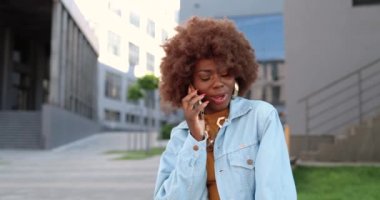 Afro-Amerikalı güzel bir kadın cep telefonuyla konuşuyor ve gülümsüyor. Cep telefonundan konuşan çekici bir kadın. Telefon görüşmesi.