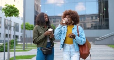 Afro-Amerikalı genç güzel kadınlar, en iyi arkadaşlar neşeyle konuşuyor ve bir fincan kahveyle şehir caddesinde yürüyorlar. Güzel mutlu kadın öğrenciler dışarıda içkilerle geziniyorlar..