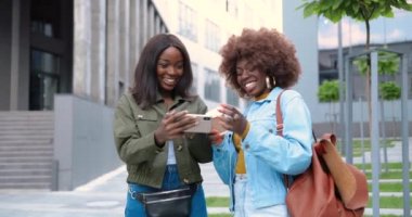 Afro-Amerikalı kadınlar konuşuyor ve şehirdeki bir sokakta cep telefonundan bir şey izliyor. Elinde bir fincan kahve olan güzel genç kadınlar akıllı telefon kullanıyor. Neşeli arkadaşlar dedikodu yapıyor. Dedikodular.