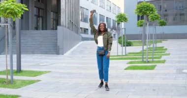 Neşeli, Afro-Amerikalı, kulaklıklı güzel bir kadın. Dans ediyor, sokaklarda yürüyor ve akıllı telefondan müzik dinliyor. Şarkı söyleyip dans eden mutlu bir kadın..