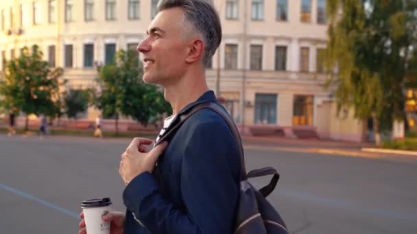 Hombre de negocios caucásico guapo de mediana edad caminando por la calle de la ciudad y bebiendo café para llevar. Hombre paseando y bebiendo bebida caliente al aire libre en la ciudad. Temprano por la mañana yendo a trabajar. — Vídeos de Stock