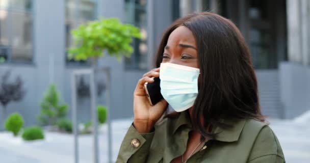戴着面具站在街上和电话交谈的非洲裔美国年轻漂亮女人。城市外的女性用手机说话。流行病或污染概念。Coronavirus. — 图库视频影像