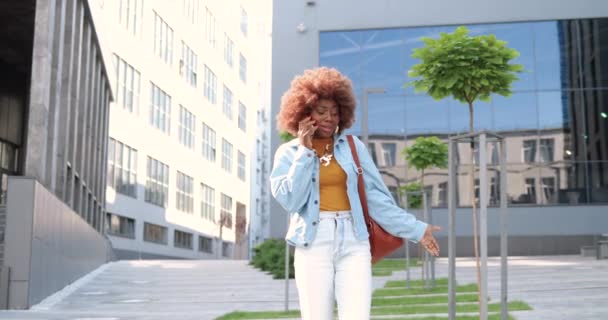 Afroamerikanerin, schöne lockige Frau, die auf dem Handy telefoniert, während sie draußen auf der Straße steht. Stylisch attraktive Frauen, die auf dem Handy sprechen. Telefonat. — Stockvideo