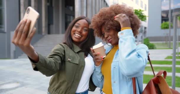 Afro-américains jeunes jolies femmes souriant joyeusement à la caméra et de prendre des photos selfie avec appareil photo de téléphone dans la rue de la ville. Belles étudiantes heureuses avec café faisant des photos avec smartphone. — Video