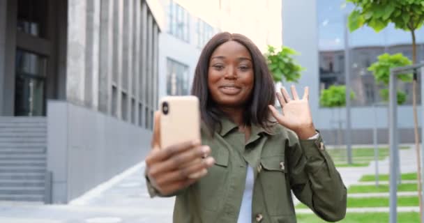 Afro-américaine belle femme souriante heureuse parlant via webcam sur téléphone mobile à l'extérieur. Joyeux vidéochat féminin sur téléphone portable et souriant. Conversation vidéo. Vidéochat. — Video