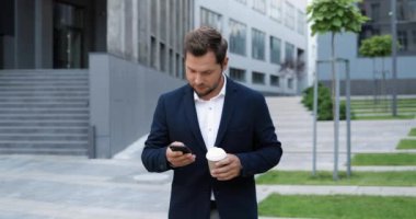 Beyaz, neşeli, şık bir genç adam sokakta yürüyor, akıllı telefonları dinliyor ya da kaydırıyor ve sabahları sıcak bir şeyler yudumluyor. Yakışıklı, mutlu, cep telefonuyla mesajlaşan ve kahve içen bir erkek. Açık hava..