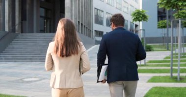 Beyaz, genç, erkek ve kadın iş ortaklarının arka tarafında. Sokakta yürüyüp sohbet ediyorlar. İş adamı ve iş kadınının arka planda gezinmesi ve sohbet etmesi.