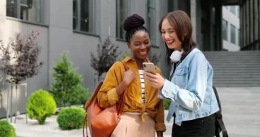 Karışık ırktan kadınlar konuşuyor ve şehirdeki bir sokakta cep telefonundan bir şeyler izliyor. Çok ırklı güzel kadınlar sohbet ediyor ve akıllı telefon kullanıyor. Neşeli arkadaşlar dedikodu yapıyor. Dedikodular.