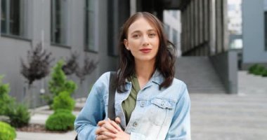 Kafkas asıllı, mavi kot ceketli, çantalı ve kameraya neşeyle gülümseyen güzel bir kadının portresi. Güzel, mutlu, açık havada neşeli bir kadın..