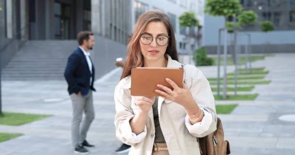 Beyaz, neşeli, stil sahibi bir kadın, şehirdeki tablet cihazını tıklatıyor ya da kaydırıyor. Güzel, mutlu bir bayanın mesaj atması ve alet bilgisayarı kullanması. Açık hava.. — Stok video