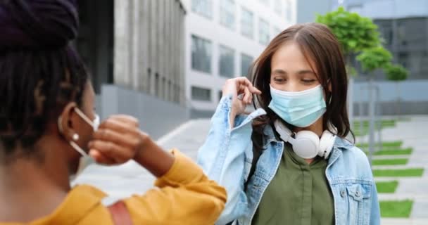 Blandade raser unga glada honor bästa vänner i medicinska masker möte på gatan och hälsning med armbågar. Multietniska glada flickor pratar och chatta glatt afroamerikanska och kaukasiska kvinnor — Stockvideo