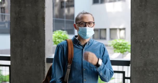 Portret van een jonge knappe mannelijke student in een bril die buiten staat, medisch masker afdoet en lacht naar de camera. Coronavirus pandemie. Blanke man op straat in bril en ademhalingsbescherming. — Stockvideo