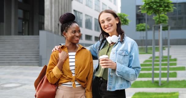 Portrait photo de jeunes jolies femmes métissées, meilleurs amis souriant joyeusement à la caméra avec une tasse de café à emporter et debout dans la rue de la ville. Multi ethnique belles femmes heureuses étudiants. — Video