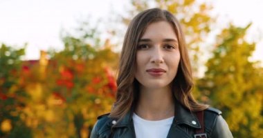 Kasabadaki parkta kameraya bakıp gülümseyen güzel beyaz, mutlu, genç bir kadının portresi. Açık havada. Güzel, neşeli bir kadın gülüşü kapanıyor sıcacık sonbaharda.