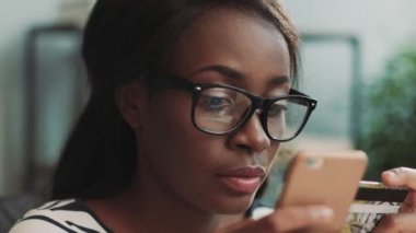 Akıllı telefon ve banka kartı tutan güzel Afro-Amerikan kızına yakın durun. Kadın kredi kartı numarasını telefonla girmiş. İnternetten alışveriş.