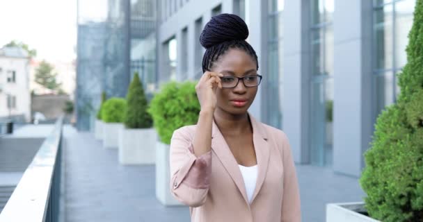 若いアフリカ系アメリカ人の美しい女性の肖像画は、眼鏡を脱いで、屋外カメラに笑みを浮かべて。ビジネスセンターの近くの通りにある魅力的な自信に満ちた幸せな陽気なビジネスマン. — ストック動画