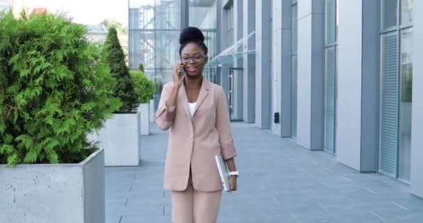 Afro-americano bella donna felice sorrise parlando sul cellulare e camminando fuori. Donna d'affari allegra che parla al cellulare e passeggia. conversazione telefonica. — Video Stock