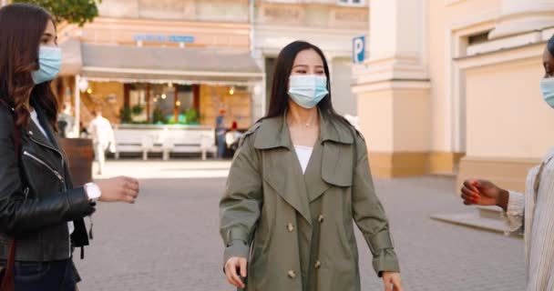 Tre giovani donne miste, migliori amici che si incontrano in strada e salutano con i gomiti durante la pandemia di coronavirus. Multi donne etniche in maschere mediche all'aperto. — Video Stock