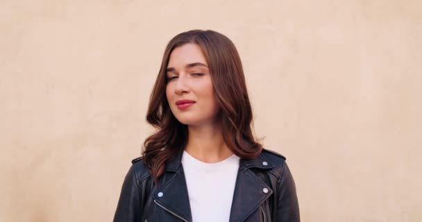 Retrato de la bella mujer caucásica joven con estilo en chaqueta de cuero negro mirando y sonriendo a la cámara en el fondo de la pared. Al aire libre. Primer plano de hermosa mujer alegre. — Vídeos de Stock