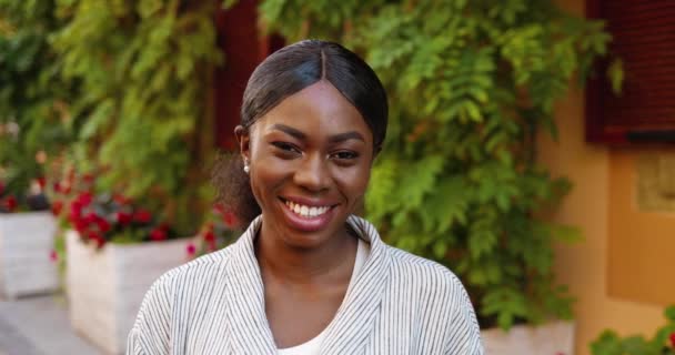Портрет гарної афроамериканської щасливої молодої жінки, яка дивиться і посміхається фотоапарату на гарній вулиці в місті. На вулиці. Зображення прекрасної радісної жіночої посмішки на зеленій стіні.. — стокове відео