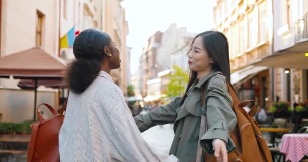 Young mixed-races beautiful joyful women meeting at street and hugging happily. Multi ethnic pretty females in hugs laughing and talking outdoor. African American and Asian girls best friends embrace. — Stock Video