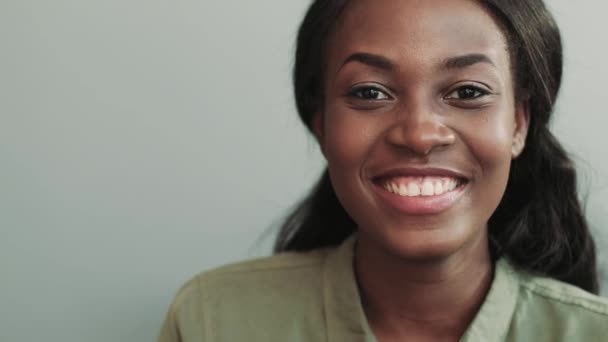 Κοντινό πλάνο πορτρέτο της νεαρής όμορφης αφροαμερικάνας γυναίκας με πράσινο πουκάμισο που κάθεται και χαμογελά κοιτάζοντας την κάμερα. — Αρχείο Βίντεο