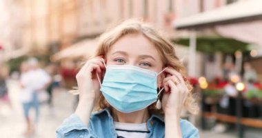 Kafkasyalı mutlu genç bir kadının portresi tıbbi maske takıyor ve sokaktaki kameraya bakıyor. Açık havada solunum koruması takan neşeli, güzel bir bayanı yakından çek. Salgın.