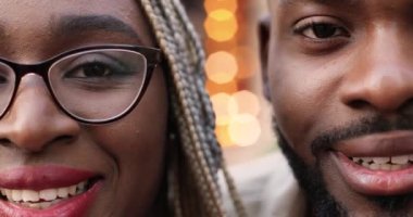 Gözlüklü, kameraya bakıp neşeyle gülümseyen Afro-Amerikan yakışıklı erkek ve güzel kadının yüzünün yarısını kapatın. Açık havada gülümseyen mutlu bir çiftin portresi..