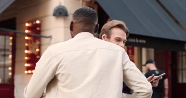 Afrika kökenli Amerikalı ve Kafkas asıllı genç erkekler yazın sokakta buluşup kucaklaşıyorlar. Neşeli erkek arkadaşlar kazara dışarıda karşılaştıklarında kucaklaşıyorlar. Karışık ırk erkekleri konuşuyor ve gülümsüyor..