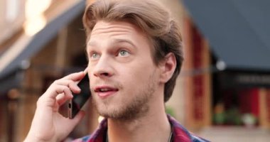 Sokakta dikilen ve cep telefonuyla konuşan Kafkasyalı genç bir adama yaklaş. Yakışıklı erkek gülümsüyor ve cep telefonuyla konuşuyor. Açık havada. Telefon görüşmesi.