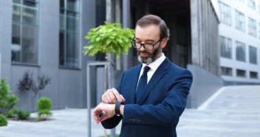 Yakışıklı beyaz iş adamı sokakta dikiliyor ve akıllı saati tıkırdatıyor. Orta yaşlı, takım elbiseli, kravat takan ve gözlüklü bir adam. Cihaz kullanıyor ve şehirde kayıyor..